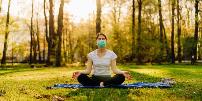 a woman wearing a mask, meditating in a sunny park