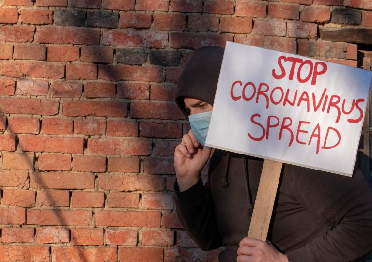 A man in a face mask carrying a sign that reads stop coronavirus spread.